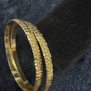 Set of four gold-toned Pure Panchaloham bangles with intricate floral and geometric traditional designs, displayed against a dark background.