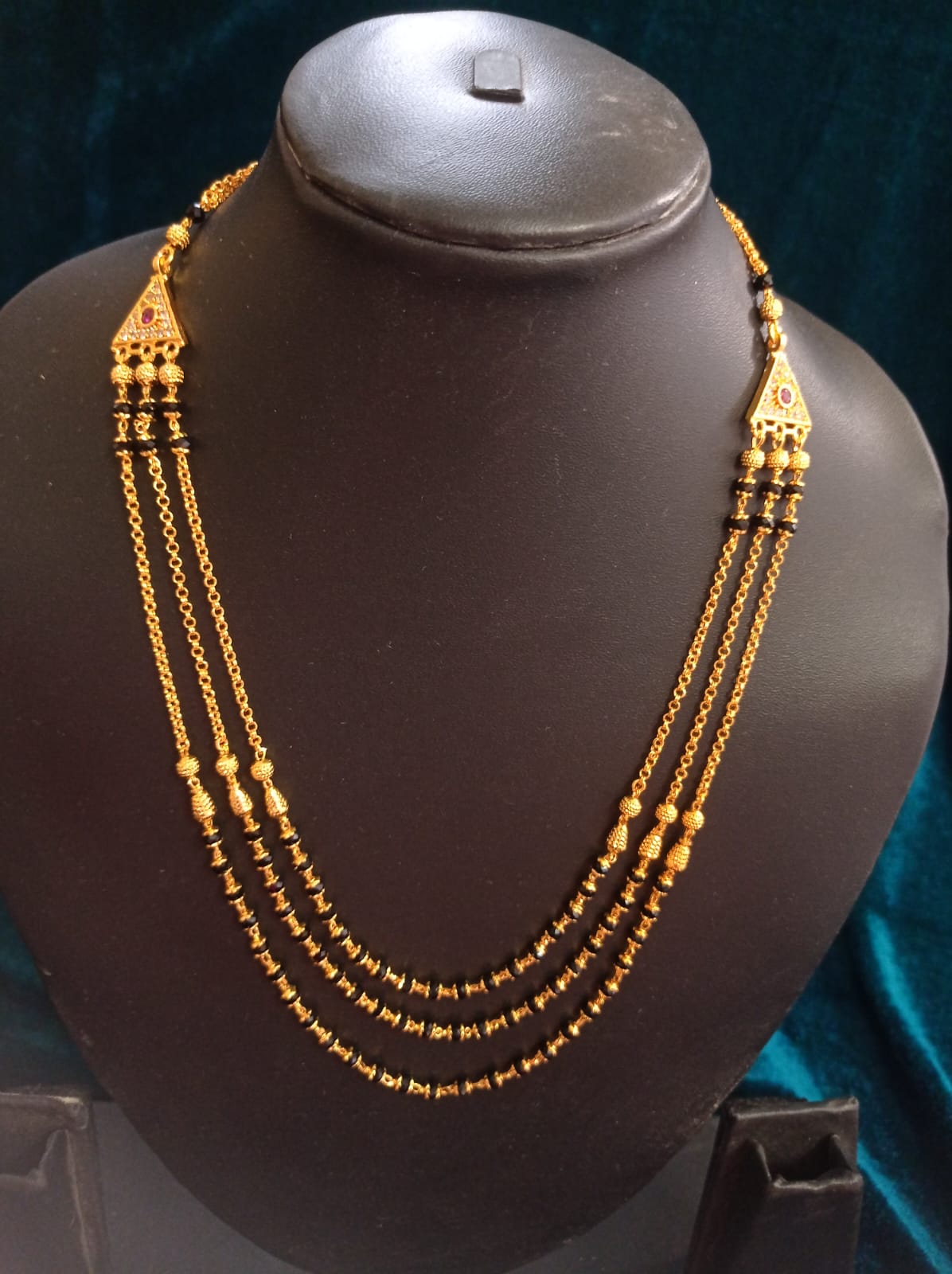 Three-layer pure Panchaloham black-bead chain with intricate gold-tone detailing, triangular motifs, and traditional red stone accents.